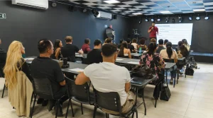 auditório corporativo cheio, palco iluminado, plateia atenta a uma apresentação.