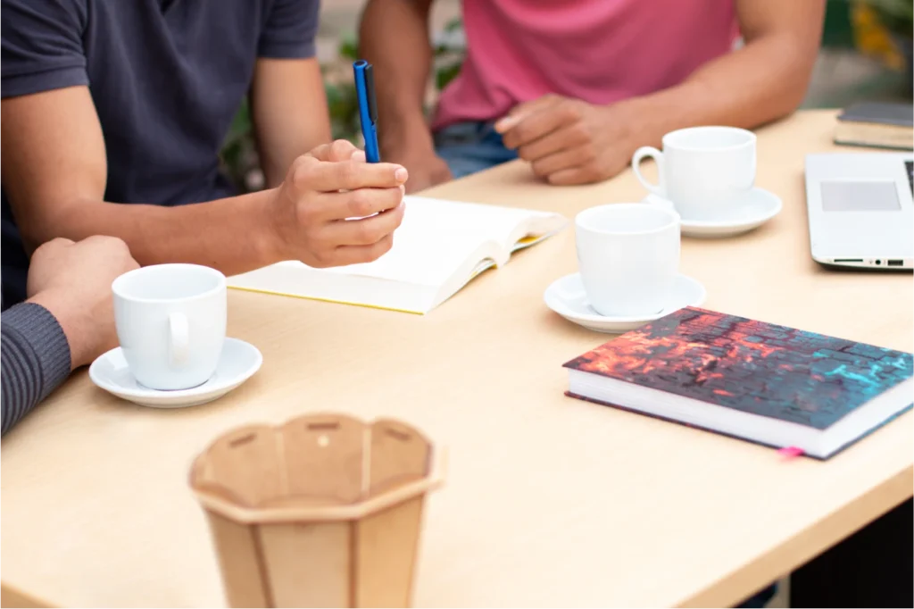 mesa de trabalho compartilhada com poucos itens (notebook, caderno, café), transmitindo simplicidade e começo de jornada.
