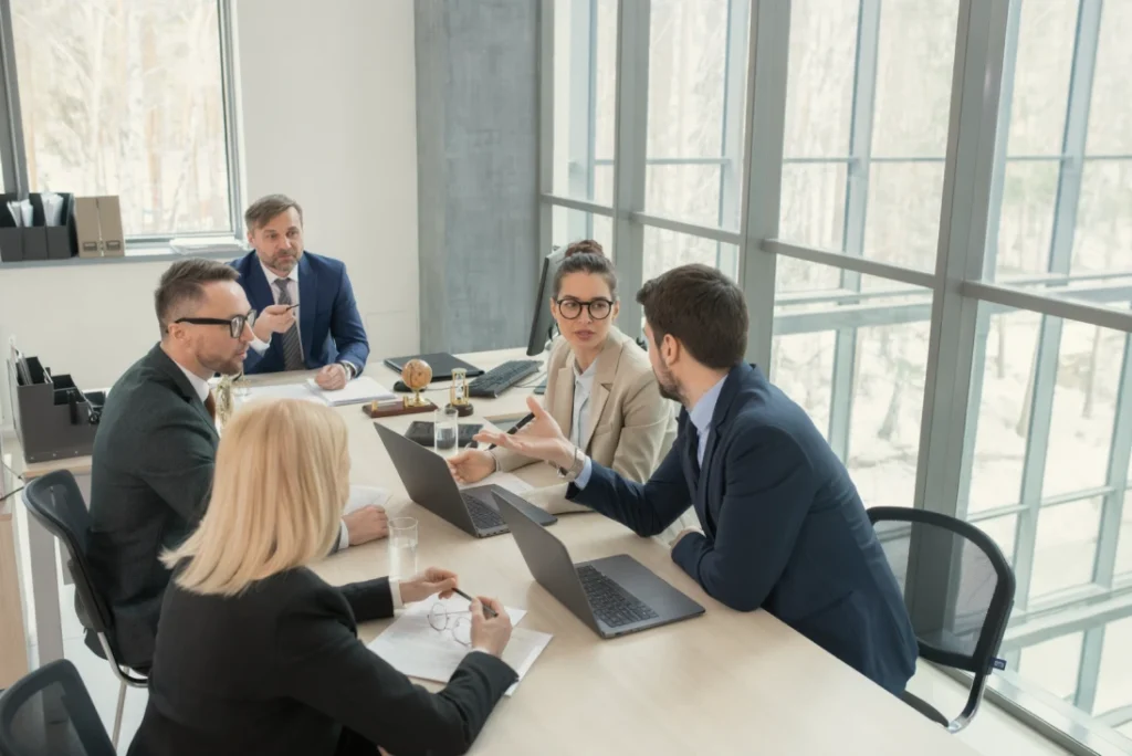 pequeno grupo sentado à mesa em conversa de negócios, expressões atentas e postura ereta.